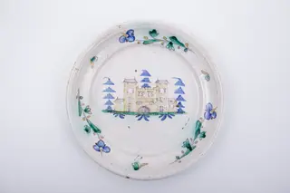 Farfurie plată,cu marginea lată și evazată spre interior. Marginea este decorată cu trei fire de floare de nu-mă-uita intercalate de un mic motiv fitomorf. Decorul central reprezintă un castel medieval poziționat într-un peisaj naturalist, înconjurat de trei brazi. Cromatică: alb, albastru, verde, maro., 1850