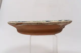 Farfurie semi-adâncă cu buza evazată și muchia rotunjită; este angobată pe suprafața interioară cu un strat de humă albă, peste care este pictat cu cornul decorul monocromatic format din motive florale stilizate și geometrice: centrul farfuriei conține un buchet format din două flori de lalea decorate cu puncte și două flori cu frunze rotunde; la baza acestui buchet este înscris anul confecționării piesei, 1782. Buza farfuriei este decorată cu un șir continuu format din linii în formă de S și grupuri de linii albastre paralele. Suprafața ornamentată a farfuriei este acoperită cu un strat de smalț transparent. Cromatica: alb, albastru., 1750