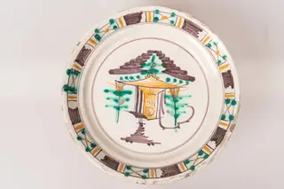 Farfurie semi-adâncă, cu buza răsfrântă. Decorul, dispus prin pictare pe un fond alb lăptos, este format dintr-un motiv arhitectural și motive vegetale stilizate, dispuse central, pe fundul farfuriei, și motive geometrice (linii galbene și dungi maro paralele, grupuri de linii intersectate sub formă de X, decorate cu puncte verzi și galbene), dispuse pe buza farfuriei, într-un registru continuu. Cele două registre ornamentale, cel central de pe fundul farfuriei și cel marginal, de pe buza acesteia, sunt încadrate în cercuri formate din linii fine de culoare maro-brun. Cromatica: alb, verde, maro-brun, galben ocru., 1850