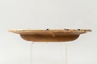 Farfurie semi-adâncă, cu buza răsfrântă; piesa este modelată la roata olarului și este angobată pe fața interioară cu humă albă. Decorul este realizat prin pictare cu pensula și se compune din motive decorative florale și vegetale stilizate, dispuse pe întreaga suprafață a piesei. La baza motivului decorativ central se află înscris anul fabricării piesei, 1782. Buza farfuriei este decorată cu un șir continuu de frunze de culoare verde și albastră. Cromatica: alb, verde, albastru. Fața decorată a farfuriei este acoperită cu un strat de smalț transparent., 1750