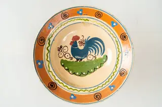 Formă adâncă, cu buză lată, răsfrântă. Piesa este modelată la roată, angobată cu humă albă. Decorul este realizat prin pictare cu pensula și cu cornul. Decorul, dispus pe întreaga suprafață a farfuriei, este format dintr-un motiv avimorf (cocoș, în zona centrală a farfuriei), motive florale și vegetale stilizate (central și pe buză) și motive geometrice (puncte, linii sub formă de cerc, linie vălurită, linie spiralată). Fața interioară a farfuriei este smălțuită cu un smalț transparent, lucios. Cromatica: alb, verde, albastru, brun, maro, siena naturală., 1850