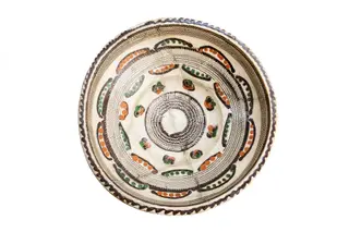 Formă tronconică; fond alb fildeșiu; pe fundul vasului este dispusă o bandă circulară lată decorată cu motivul specific centrului: pînza de păianjen - realizată prin tehnică jirăvirii cu gaița, încadrată de boboci de floare stilizați, colorați în verde și cărămiziu și linii ușor curbate care au interior puncte de culoare cărămizie, respectiv: verde. Pe umărul vasului este dispusă o altă bandă circulară jirăvită cu motivului pînzei de păianjen care prezintă în exterior linii curbe similare cu cele descrise mai sus. Întreaga compoziție sugerează un soare stilizat. Buza este decorată cu un val circular de culoare brună. Piesa reprezintă una dintre primele achiziții ale lui Alexandru Tzigara Samurcaș. Folosită la decorarea interiorului țărănesc în așa numita - cameră bună