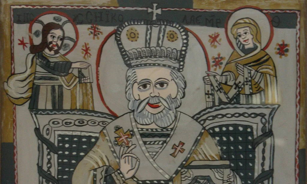 Sfântul ierarh Nicolae așezat pe un tron bogat ornamentat, de factură barocă, binecuvântează cu dreapta (prin unirea inelarului cu degetul mare), cu stânga sprijină Evanghelia pe a cărei copertă este redat un serafim. În colțurile de sus sunt reprezentați Iisus Hristos, ținând Evanghelia pe care o întinde sfântului și Maica Domnului având pe brațe cinstitul ei brâu. În jurul capului Mântuitorului este trasat nimbul cruciger cu însemnele consacrate. Sfântul Nicolae este reprezentat bătrân, părul și barba albe, ondulate, scurte. Veșminte arhirești: stiharul și sacosul în tonuri de galben și negru. Epitrahilul (patrafirul) brodat cu motivul crucii, în partea de jos un serafim. Mitra înaltă, bipartită, surmontată de cruce. Pe poalele sacosului decor floral. Aureolele trasate cu roșu, linie dublă. Dispunerea personajelor ușor asimetrică. Chenar pe trei laturi, benzi în culori alternante, care se regăsesc în cromatica icoanei. Rama este băițuită; culoarea: brun. Cromatica: gri, roșu, galben, ocru, negru, fond: gri - argintiu., by Lupu Ana