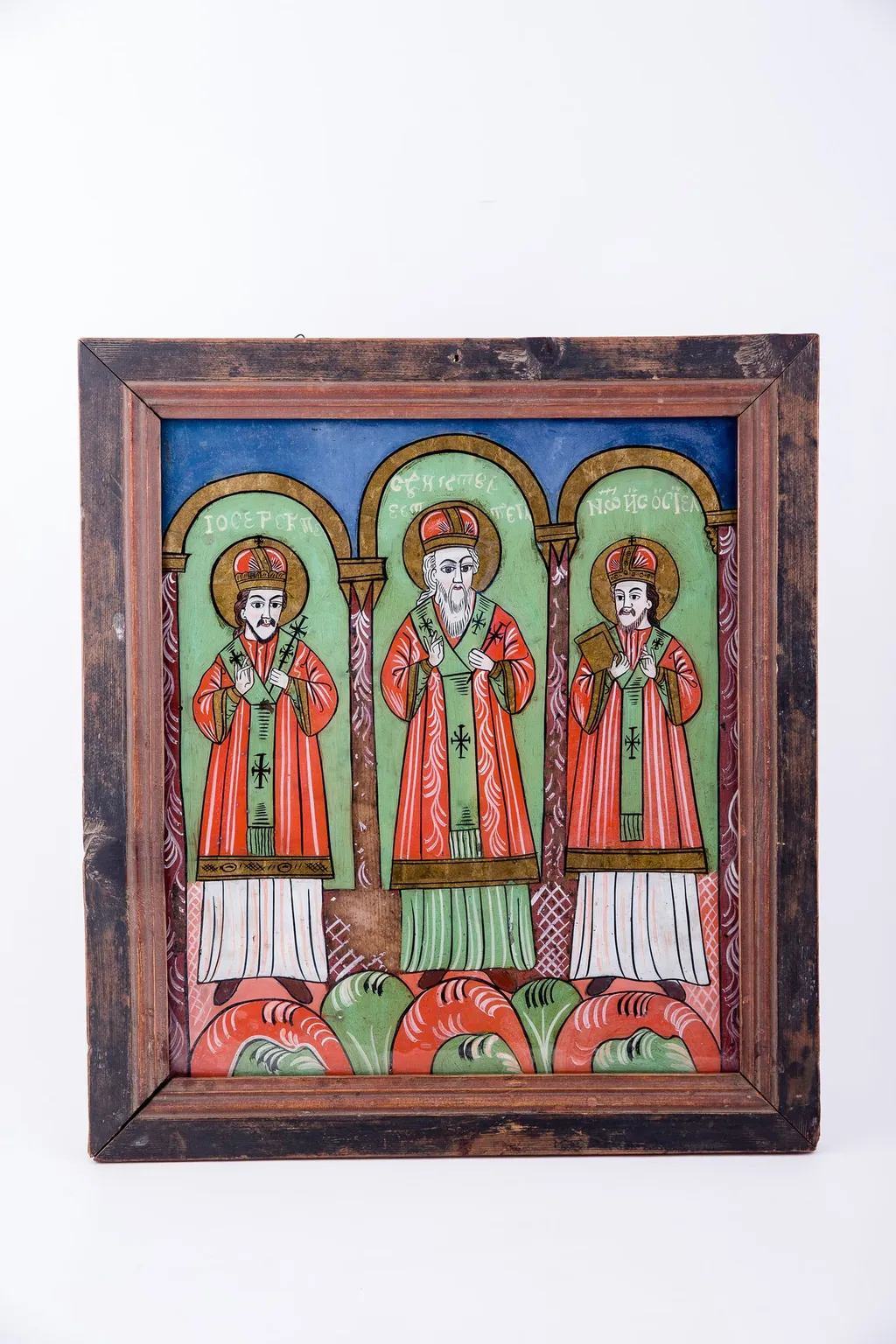 Cei Trei Sfinți Ierarhi Vasile cel Mare, Grigorie de Dumnezeu Cuvântătorul și Ioan Gură-de-Aur slujesc și săvârșesc Sfânta Liturghie împreună. Sunt înveșmântați în veșminte liturgice: sacos verde-alb-verde, felon roșu vermillon, epitrahil verde cu câte patru cruci. Sfântul Vasile cel Mare are Sfânta Evanghelie în mâna dreaptă. Sfântul Ierarh Grigorie de Dumnezeu Cuvântătorul Binecuvintează. Cei trei Sfinți Ierarhi stau cu picioarele pe perinițe rotunde de culori alternative: roșu, verde, alb. Fiecare sfânt ierarh este încadrat de două coloane și o boltă de biserică. Sunt prezente elemente arhitectură bisericească. Fondul registrului superior este albastru. Cromatica este luminoasă și armonioasă: verde, alb, roșu vermillon, roșu, albastru, negru. Este o icoană specifică picturii de Țara Făgărașului, cu un desen fin cu conturul negru și cromatica pastelată. După stilul picturii întregii compoziții, icoane poate să aparțină lui Matei Țimforea., by Matei Țimforea