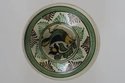 Blid de formă tronconică, adâncit, cu buza înălțată și ușor evazată. Este smălțuit în interior și în exterior (buza). Decorat la interior cu motive avimorfe și fitomorfe, încadrate de două cercuri concentrice; pe margine, în interior este decorată cu linii și brăduț stilizat, iar în exterior cu două linii; pe fund are două găuri pentru agățare. Cromatică: fond: gri (exterior); alb (interior); motive: maro; verde; galben; negru.