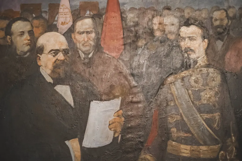 Lucrare având în planul apropiat pe domnitorul Al. I.Cuza și M. Kogălniceanu aflați într-o încăpere. Prințul este în uniformă militară și ține în una din mâini un document rulat. Are în față o masă îmbrăcată în catifea verde. Kogălniceanu este îmbrăcat în costum negru, cămașă albă și legătură neagră la gât. Are în una din mâini, foile albe probabil ale Actului de inaugurare. În spate lor se află o mulțime de chipuri (din care se face remarcată figura Mitropolitului ) și două steaguri (roșu și alb - cel al Universității). Nu este semnat și nici datat., by pictor Dan Hatmanu, unspecified