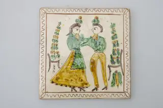 Piesă ceramică de formă pătrată, smălțuită și angobată, cu rol decorativ. Laturile pătratului sunt marcate de două chenare, primul vălurit, al doilea în linie dreaptă. Ornamentată cu motive antropomorfe și floral-vegetale: doi tineri, un băiat și o fată ținându-se pe după mijloc (băiatul cu mâna dreaptă, fata cu stânga). În spatele lor câte un scaun din care se înalță o floare. Motivele au fost la început incizate, iar apoi pictate. Pe spate, cahla este prevăzută cu un orificiu pentru prinderea aței. Tot aici, este inscripționat numele meșterului olar, "Colibaba". Cromatică: fundal alb; motive: verde, galben, cărămiziu, maro, negru.