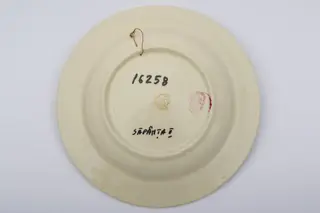 Piesă ceramică smălțuită, de formă circulară, cu baza plată, pereții puțin înălțați și marginile larg evazate. Peste stratul alb de angobă a fost pictat decorul fitomorf stilizat. Central, pe fundul piesei au fost realizați trei trandafiri roșii, însoțiți de patru boboci roșii și frunze verzi. Primul registru este încadrat de cel de-al doilea registru, dispus pe marginea recipientului ceramic. O bandă circulară galbeană peste care au fost realizați șase boboci roșii și frunze maro și verzi, este mărginită de două linii concentrice drepte. Farfuria era folosită în gospodărie pentru servirea hranei sau amenajarea interioarelor. Prezintă uzură funcțională. Cromatică: fond: alb; motive: roșu; verde; galben; maro.