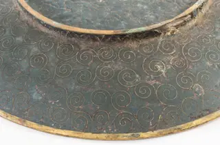 Piesă din metal pictat, incizat, de formă rotundă, puțin adâncită, cu fundul supraînălțat printr-un brâu circular. Decorul este dispus pe toată suprafața piesei, atât pe față (motive pictate: central, un buchet de crizanteme cu frunze, alături de fluturi; pe margine, un brâu circular cu motive de forma evantaiului), cât și pe spate (compoziție compactă de spirale incizate). Cromatică: albastru, verde, galben, negru, grena, roz, mov, violet, maro, alb.