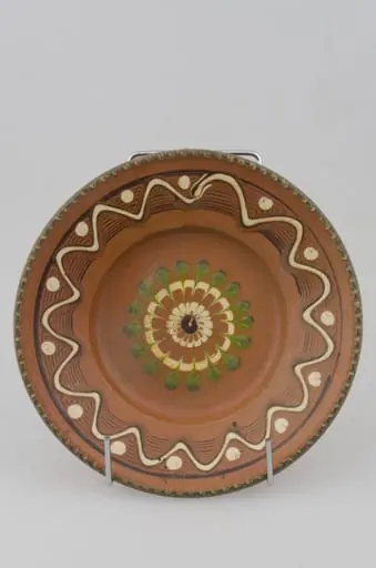 Farfurie cu pereții rotunjiți, marginea oblică lată și buza crestată. Prezintă decor geometric pe margine: linii frânte și curbe; pete de culoare; central avem o floare stilizată. Cromatică: fond: maro; motive: verde; alb., by Răducanu Ion
