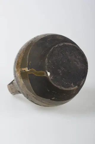 Recipient ceramic de formă sferică cu o toartă ce pornește de la baza buzei, printr-un inel, și se prinde de corp deasupra diametrului maxim. Buza este înaltă și relativ îngustă. Decorul este compus din motive geometrice (liniare, curbilinii) pictate, plasate pe toată suprafața obiectului. Pe alocuri sunt prezente pete de smalț. Vasul este smălțuit la exterior. Cromatică: fond: maron; bej; motive: maron închis, verde, galben.