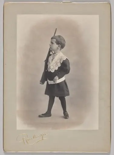 Untitled (young boy with lace collar and toy rifle), by Reutlinger Studios