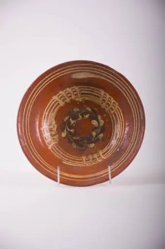 Farfurie de formă tronconică, marginea lată ușor înclinată în sus. Decor: pe fond de roșeală pe fundul plat, un cerc de puncte albe și negre în formă de coroniță; pe perete cercuri concentrice cu motive de linii verticale, pe margine trei cercuri concentrice albe. Smalț incolor. Cromatică: fond: maro; motive: alb-gălbui; negru., by Rovența Vasile
