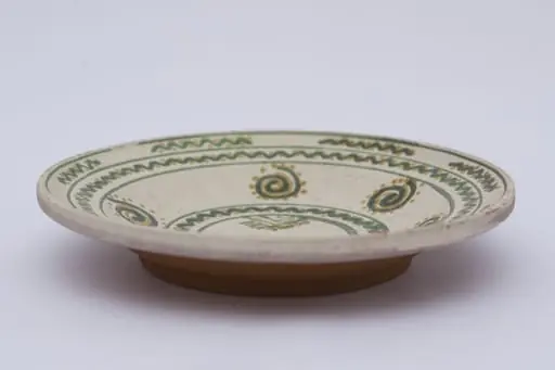 Vas ceramic de formă discoidală pe bază puțin înălțată. Fața farfuriei a fost introdusă în angobă albă, decorația a fost făcută cu pensula. Pe fundul vasului sunt două cercuri concentrice: în primul sunt doi brăduți, iar în al doilea valul punctat. Pe pereți sunt șase spirale punctate. Marginea vasului a fost împărțită în două registre, primul cu val punctat, în al doilea sunt șapte valuri întrerupte. La posterior, pe fund, semătura ”D Șchiopu ''. Pentru atârnare baza este perforată. Cromatică: fond: alb; motive; verde; galben., by Șchiopu Dumitru