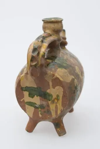 Recipient ceramic sub formă de butoiaș cilindric, dispus pe orizontală, asemănător corpului de rață. Sprijinit pe patru picioare tubulare dispuse oblic câte două la capete. Prezintă toartă. Scurgere printr-un cioc cu vârful conic care este legat prins printr-un inel de mijlocul gâtului cilindric și strâmt dispus la mijlocul vasului, având la capăt reliefată o față umană în relief terminată cu gura cu buză dreaptă pentru introducerea lichidelor. Opus ciocului, prezintă o toartă lată, puternic arcuită, de-a lungul căreia se suprapune, o bandă reliefață decorată prin presare cu degetul. Pe corpul vasului, dispuse aleatoriu, pete albe și de smalț verde și galben. Cromatică: fond: cărămiziu; motive: alb; galben; verde., by Țepeniș Dumitru