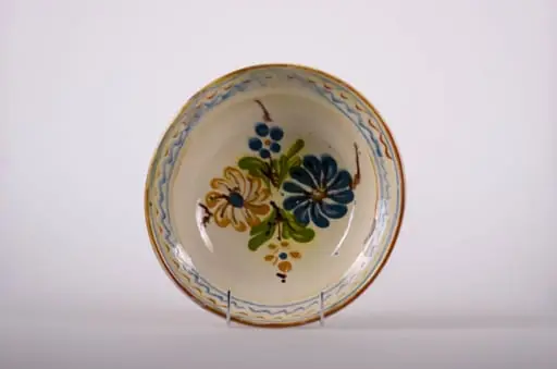 Blid de formă tronconică, adâncit; pe fund are găuri pentru agățare. Este smălțuit în interior și exterior (buza); este decorat cu motive geometrice: linie, linie ondulată; motive fitomorfe: frunze; motive florale. Cromatică: fond: alb; motive: albastru; maro; verde., by Unknown