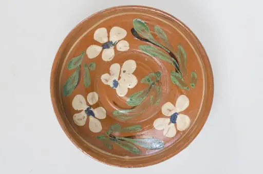 Blidul de formă tronconică adânc, smălțuit (la interior). Acesta este ornamentat cu motive florale, având cu buza înaltă. Blidul este neornamentat la exterior, fiind smălțuit (la exterior) doar pe buză. Pe exteriorul buzei este incizată o linie. Fundul obiectului are formă circulară, fiind prevăzut cu două orificii pentru prindere. Cromatică: fond: cărămiziu (exterior); alb (interior); decor: verde; alb; albastru; maro., by Unknown