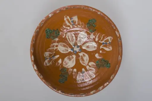 Blidul de formă tronconică este unul adânc, smălțuit pe interior, ornamentat cu motive florale, cu buză înaltă, neornamentat la exterior. Obiectul este smălțuit, la exterior, doar pe buză. Acesta prezintă puncte pictate cu pensula pe buză, la interior. Blidul este prevăzut cu două orificii pentru prindere, pe fund. Cromatică: fondul este cărămiziu, iar motivele sunt pictate cu alb, verde și albastru., by Unknown