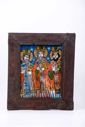 Cei Trei Sfinți Ierarhi Vasile cel Mare, Grigorie de Dumnezeu Cuvântătorul și Ioan Gură-de-Aur slujesc și săvârșesc Sfânta Liturghie împreună. Sunt înveșmântați în veșminte liturgice: sacos crem-albastru-alb-crem, felon roșu vermillon, epitrahil albastru-verde cu câte patru cruci negre. Sfântul Vasile cel Mare are Sfânta Evanghelie în mâna dreaptă. Sfântul Ierarh Grigorie de Dumnezeu Cuvântătorul Binecuvântează. Fondul registrului superior este cerul albastru-regal, bogat ornamentat cu elemente astrale - stele roșii și albe. Cromatica este luminoasă și armonioasă: verde văratic, alb, roșu vermillon, galben-ocru, bej, crem, albastru regal și bleu-ciel, negru. Este o icoană specifică picturii de Țara Oltului, cu un desen fin cu conturul negru și cromatica pastelată. Inscripția din româno-chirilică se traduce Vasile Grigorie Ioan., by Unknown, 1850