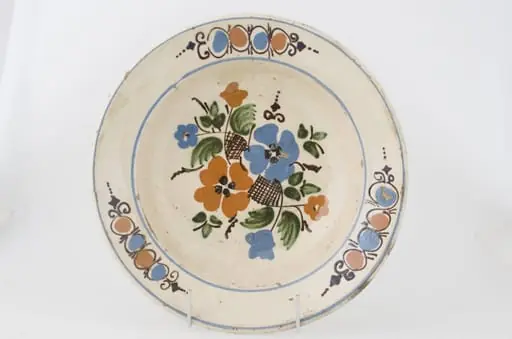Farfuria este lucrată la roată, prezintă marginea evazată în plan orizontal fiind smălțuit în interior. Pe suprafața interioară a vasului se identifică registre decorative floral-vegetale dispuse pe fundul vasului și pe marginea interioară. Registrele sunt delimitate de două cercuri realizate prin pictare și dispuse pe buza vasului și spre interiorul acestuia. Cromatică: fond: alb; motive: roșu; albastru; verde; brun; maro., by Unknown