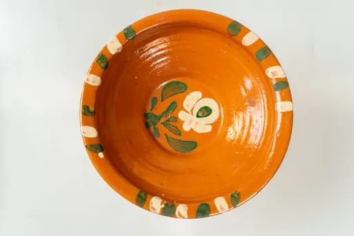 Farfurie adâncă, corpul de formă tronconică, cu buză îngustă, răsfrântă. Piesa este modelată la roata olarului, nefiind angobată. Decorul este realizat prin pictare cu pensula și constă în motive decorative florale (o floare cu frunze), dispuse central, pe fundul farfuriei și motive geometrice (linii groase, paralele), dispuse în trei registre, pe buza acesteia. Cromatica decorului: alb, verde. Farfuria este smălțuită pe interior, cu smalț transparent., by Unknown
