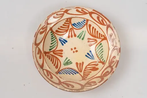 Farfurie adâncă, cu buză relativ îngustă, evazată; este acoperită pe suprafața interioară cu un strat de angobă albă, peste care este pictat cu cornul decorul format din motive geometrice: fundul farfuriei și peretele acesteia este decorat cu motive formate din linii curbe de culoare maro, ce au pe suprafața interioară linii oblice paralele, inegale ca mărime, de culoare verde, albastru, maro; grupuri de câte trei linii colorate, în formă de V și patru puncte centrale, de culoare maro. Buza farfuriei este decorată cu un șir continuu din motive formate din linii ovale, de culoare maro, cu câte două linii sub formă de virgulă în interior. Suprafața ornamentată a farfuriei este acoperită cu un strat de smalț transparent. Cromatica: alb, albastru, verde, maro., by Unknown