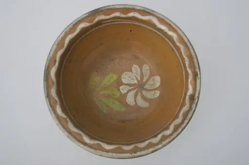 Farfurie adânca, de formă tronconică, smălțuită în interior. Pe margine prezintă decor geometric: linia vălurită; central o floare. Cromatică: fond: cărămiziu; motive: alb; verde; albastru., by Unknown