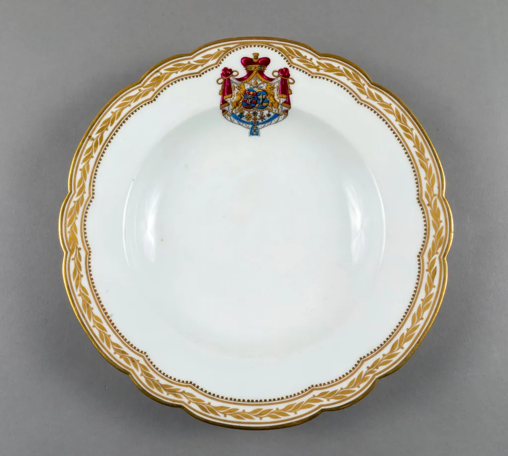 Farfurie adâncă de porțelan de Sevres, realizată din porțelan alb, cu margini treflate, decorate cu frunze de laur pictate, în centrul decorațiilor având blazonul familiei Suțu. Blazonul a fost adesea confundat cu cel al Principatelor Unite, fiind format din: stemele celor două țări românești: prima cea a Moldovei, cea de-a doua cea a Țării Românești, steme plasate pe două scuturi ovale, în fascie, acolate, puțin suprapuse, cea a Moldovei având capul de bour de argint cu stea în șase colțuri de aur, pe un scut cu segmente verticale egale roșii și albastre; cea a Țării Românești având acvila cruciată de argint, cu crucea de aur, scutul având segmente verticale galbene și albastre. Cele două scuturi au ca tenanți doi lei aurii, deasupra armele familiei Suțu – iataganul și sabia, ambele aurii, precum, pe un pavilion de purpură căptușit cu hermină, brodat cu ciucuri de aur și prins într-o coroană cu pietre scumpe. Pe scut, în partea inferioară se află și decorațiile familiei Suțu. Familia Suțu a fost o familie fanariotă grecească, venită în principate în cea de-a doua parte a secolului al XVIII-lea, având trei domni în ambele țări Românești (Alexandru Suțu, Mihai Suțu și Grigore Suțu). Blazonul familiei poate fi admirat inclusiv pe clădirea Palatului Suțu, astăzi Muzeul de Istorie a Municipiului București. Farfuria are marca atelierului Sevres și modelul din anul 1844, precum și seria., by Unknown, 1850
