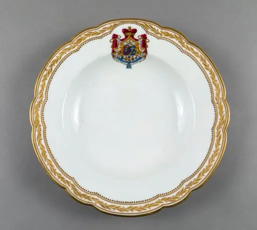 Farfurie adâncă de porțelan de Sevres, realizată din porțelan alb, cu margini treflate, decorate cu frunze de laur pictate, în centrul decorațiilor având blazonul familiei Suțu. Blazonul a fost adesea confundat cu cel al Principatelor Unite, fiind format din: stemele celor două țări românești: prima cea a Moldovei, cea de-a doua cea a Țării Românești, steme plasate pe două scuturi ovale, în fascie, acolate, puțin suprapuse, cea a Moldovei având capul de bour de argint cu stea în șase colțuri de aur, pe un scut cu segmente verticale egale roșii și albastre; cea a Țării Românești având acvila cruciată de argint, cu crucea de aur, scutul având segmente verticale galbene și albastre. Cele două scuturi au ca tenanți doi lei aurii, deasupra armele familiei Suțu – iataganul și sabia, ambele aurii, precum, pe un pavilion de purpură căptușit cu hermină, brodat cu ciucuri de aur și prins într-o coroană cu pietre scumpe. Pe scut, în partea inferioară se află și decorațiile familiei Suțu. Familia Suțu a fost o familie fanariotă grecească, venită în principate în cea de-a doua parte a secolului al XVIII-lea, având trei domni în ambele țări Românești (Alexandru Suțu, Mihai Suțu și Grigore Suțu). Blazonul familiei poate fi admirat inclusiv pe clădirea Palatului Suțu, astăzi Muzeul de Istorie a Municipiului București. Farfuria are marca atelierului Sevres și modelul din anul 1844, precum și seria., by Unknown, 1850