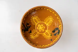 Farfurie adâncă de tip castron, cu baza îngustă, corp tronconic și buză dreaptă. Piesa este modelată la roata olarului, nefiind angobată. Decorul este pictat cu cornul cu humă albă și se compune din motive florale geometrizate (rozetă centrală, patru linii ovale dispuse sub formă de petale, decorate pe exterior cu linii paralele, ca niște raze și cu puncte în interior); partea inferioară a buzei este marcată cu o linie ondulată dispusă sub formă de cerc. Peste decor au fost stropite cu pensula pete de culoare verde-închis (două zone de pete diametral opuse pe peretele vasului). Pe partea exterioară a farfuriei, în zona buzei, a fost pictată cu cornul o linie ondulată de culoare albă. Fața ornamentată a farfuriei și zona exterioară a buzei sunt acoperite cu un strat de smalț galben transparent., by Unknown, 1850