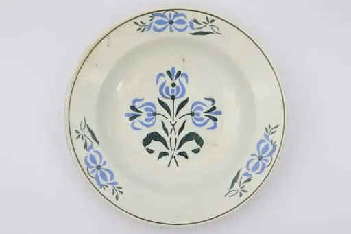 Farfurie cu fundul plat, puțin adâncit. Pe fundul vasului decor ilustrând un buchet de flori albastre cu tulpini și frunze verzi. Pe marginile vasului dispuse câte trei grupuri a două flori ca și cele de pe fund. La buză o linie neagră dispusă circular.. La posterior pe inelul de susținere practicate două perforații pentru atârnare. Cromatica: fond: alb; motive: albastru, verde, negru., by Unknown