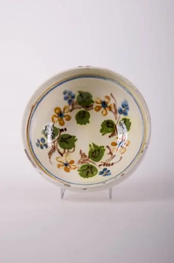 Farfurie de formă tronconică, adâncită, cu buza foarte înaltă; pe fund are găuri pentru agățare. Este smălțuit în interior și exterior (buza). Decorat cu motive geometrice: linie; motive fitomorfe; motive florale. Cromatică: fond: alb; motive: verde; maro; albastru., by Unknown