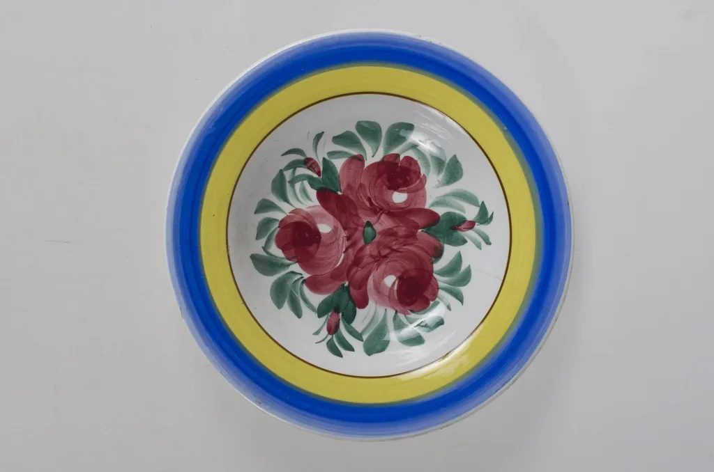 Farfurie de formă tronconică, adâncită; motive florale în centru (trandafiri); pe margine este decorat cu trei cercuri concentrice. Pe fund este o ștanță: o casă cu o pasăre pe acoperiș cu inscripție deasupra: ”MAGYAR” și dedesubt: ”1971” și un cuvânt indescifrabil. Pe fundul vasului sunt două incizii în care este introdus un șnur folosit la agățarea vasului pe perete. Vasul este smălțuit interior-exterior. Decor obținut prin pictare. Cromatică: fond: alb, motive: roșu; verde; albastru; galben., by Unknown, 1850