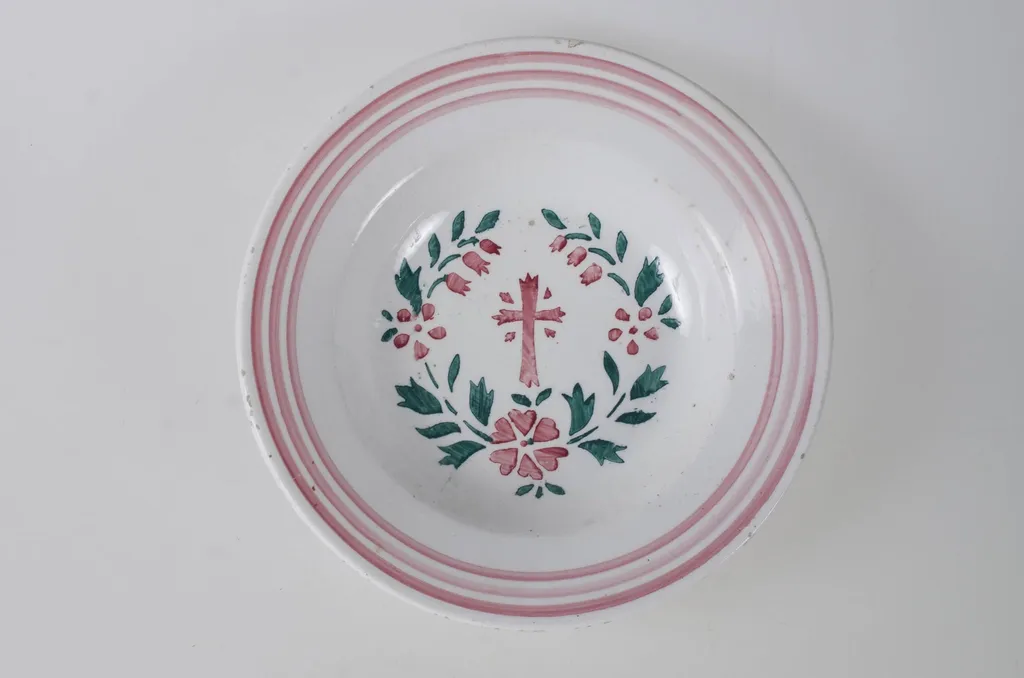 Farfurie de formă tronconică, adâncită; pe margine este decorată cu motive geometrice: trei cercuri concentrice. În centru este pictată o cruce, încadrată de flori și frunze dispuse circular. Pe exteriorul vasului de la bază spre buză se disting trei profile circulare. Cromatică: fond alb; motive: roșu; verde., by Unknown, 1850