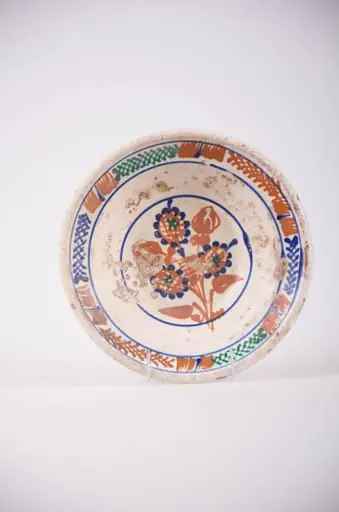 Farfurie de formă tronconică cu deschidere mare. Smălțuit în interior și ornamentat cu motive geometrice: cercuri; motive florale, pete de culoare și motiv vegetal: brăduț. Motivul floral se află pe fundul vasului și este înscris într-un cerc. Motivele vegetale și petele de culoare sunt amplasate pe marginea farfuriei și sunt încadrate de două cercuri. Cromatică: fond: alb; motive: maro; verde; albastru., by Unknown