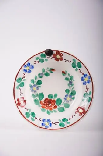 Farfurie de porțelan smălțuită pe fond alb. Decorată cu flori și frunze dispuse sub formă de ghirlande atât în centrul vasului cât și pe buza acestuia. De asemenea sunt prezente și motive geometrice: linia și linii întrerupte. Comatică: fond: alb; motive: verde; albastru; galben; roșu., by Unknown