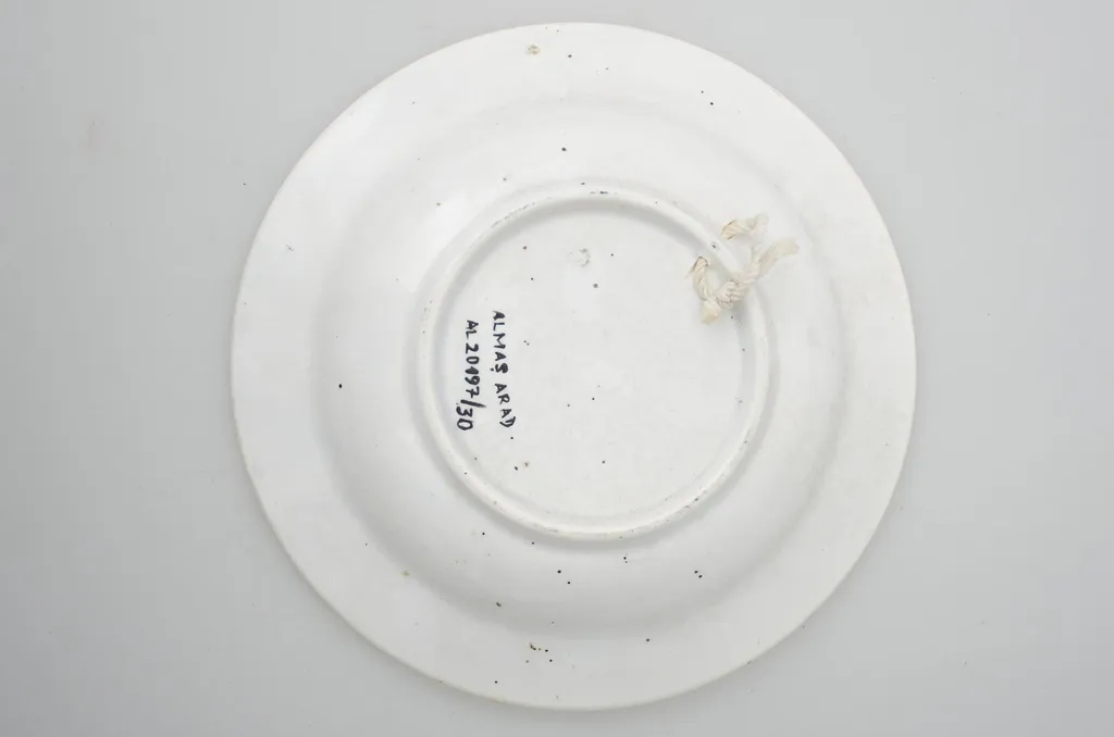 Farfurie din porțelan, de formă tronconică, întrebuințată în gospodărie la decorarea pereților casei. În interior se identifică un decor fitomorf, motive florale și vegetale, precum și un decor geometric. Motive florare sunt dispuse în trei registre pe margine, încadrate de un cerc negru; în centru este decorat cu trei flori albastre cu frunze verzi. Cromatică: fond: alb; motive: albastru, negru, verde., by Unknown, 1850
