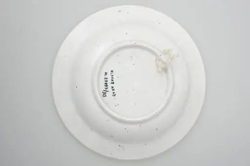 Farfurie din porțelan, de formă tronconică, întrebuințată în gospodărie la decorarea pereților casei. În interior se identifică un decor fitomorf, motive florale și vegetale, precum și un decor geometric. Motive florare sunt dispuse în trei registre pe margine, încadrate de un cerc negru; în centru este decorat cu trei flori albastre cu frunze verzi. Cromatică: fond: alb; motive: albastru, negru, verde., by Unknown