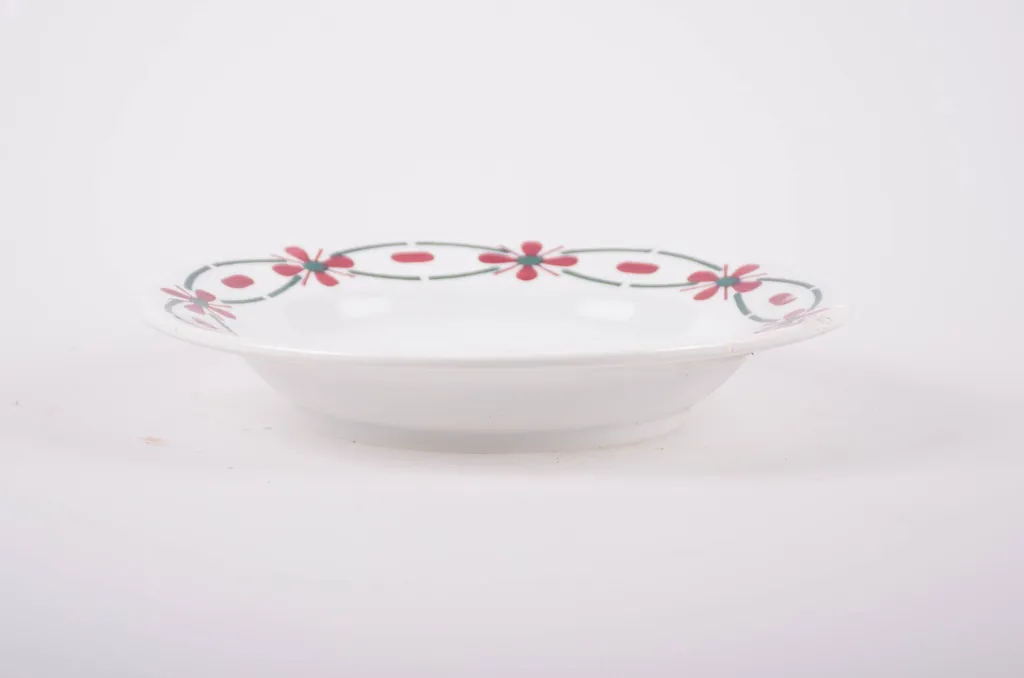 Farfurie din porțelan de formă tronconică. Pe fond alb, marginea este decorată cu flori stilizate. Cromatică: roșu și verde; interiorul farfuriei prezintă flori în: roșu; albastru; verde., by Unknown, 1950