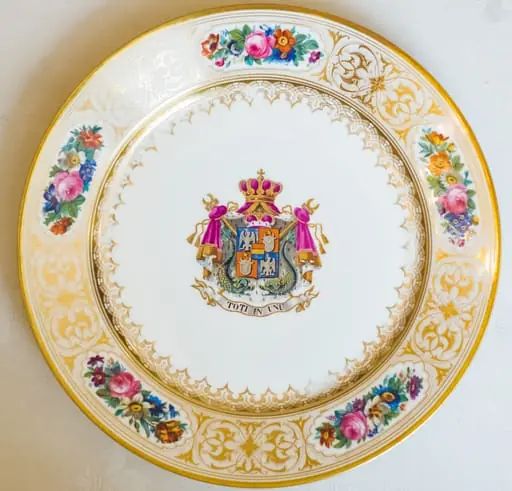 Farfurie, model decorativ stil Louis-Philippe, ales pentru serviciul de masa de peste 100 de piese Cuza, comandat la manufacturile regale din Sevres. Acesta urma să fie folosit de familia domnitoare Cuza în palatul de la Cotroceni. Farfuria este întinsă, circulară, pictată pe margini cu cinci medalioane florale care alternează cu arabescuri aurii. Este decorată central cu stema Principatelor Române și deviza unionistă „Toți în Unu". Stema și motivele florale se caracterizează printr-o vie policromie: galben, auriu, nuanțe de roșu, roz, verde și albastru. Pe reversul ei apar două marci în câmp circular: „Chateaux de Trianon" (culoare roșu carmin) și „Sevres 1846" (cu albastru). De asemenea, se remarcă cartelul care conține, în cifre latine, datele dublei alegeri a lui Al. I. Cuza ca principe al Moldovei și Țării Românești., by Unknown