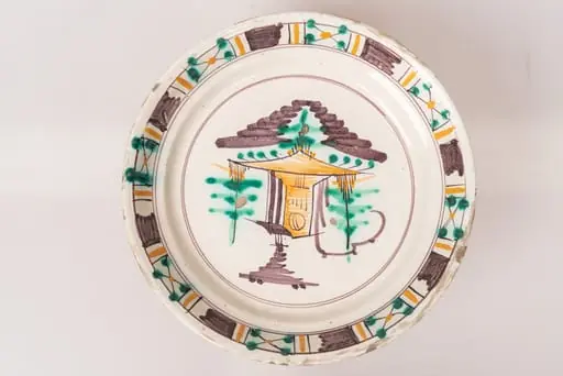 Farfurie semi-adâncă, cu buza răsfrântă. Decorul, dispus prin pictare pe un fond alb lăptos, este format dintr-un motiv arhitectural și motive vegetale stilizate, dispuse central, pe fundul farfuriei, și motive geometrice (linii galbene și dungi maro paralele, grupuri de linii intersectate sub formă de X, decorate cu puncte verzi și galbene), dispuse pe buza farfuriei, într-un registru continuu. Cele două registre ornamentale, cel central de pe fundul farfuriei și cel marginal, de pe buza acesteia, sunt încadrate în cercuri formate din linii fine de culoare maro-brun. Cromatica: alb, verde, maro-brun, galben ocru., by Unknown