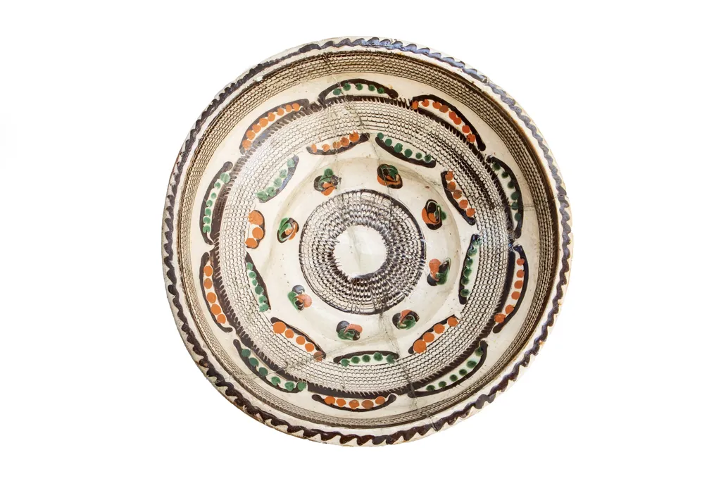 Formă tronconică; fond alb fildeșiu; pe fundul vasului este dispusă o bandă circulară lată decorată cu motivul specific centrului: pînza de păianjen - realizată prin tehnică jirăvirii cu gaița, încadrată de boboci de floare stilizați, colorați în verde și cărămiziu și linii ușor curbate care au interior puncte de culoare cărămizie, respectiv: verde. Pe umărul vasului este dispusă o altă bandă circulară jirăvită cu motivului pînzei de păianjen care prezintă în exterior linii curbe similare cu cele descrise mai sus. Întreaga compoziție sugerează un soare stilizat. Buza este decorată cu un val circular de culoare brună. Piesa reprezintă una dintre primele achiziții ale lui Alexandru Tzigara Samurcaș. Folosită la decorarea interiorului țărănesc în așa numita - cameră bună, by Unknown, 1850