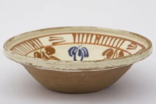 Piesă ceramică de dimensiuni medii, smălțuit la interior, având formă tronconică, cu baza plată, pereții ridicați și buza evazată. Întreaga suprafață interioră a piesei a fost decorată cu motive geometrizante și fitomorfe stilizate. O floare, cu petale verzi, roșii și albastre și cu un punct roșu în mijloc, este mărginită de un brâu circular, compus din opt reprezentări florale, cu aceiași cromatică. Marginal, pe buza piesei a fost realizat cel de-al doilea registru: două linii circulare, care încadrează patru registre, compuse din linii verticale, despărțite de alte patru registre din linii orizontale (2-3 linii). Farfuria era folosită în gospodărie pentru decorarea interioarelor. Prezintă uzură funcțională. Cromatică: fond: cărămiziu (exterior); crem (interior); motive: roșu; albastru; verde., by Unknown