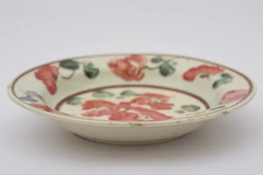 Piesă ceramică smălțuiță de dimensiuni reduse și formă cilindrică, cu baza plată și susținută de un inel circular, pereții ușor ridicați și buza larg evazată. Suprafața interioară a recipientului a fost ornamentată cu două registre decororative cu motive geometrizante și fitomorfe stilizate. Central, pe fundul vasului au fost pictați trei flori roșii cu frunze verzi, cel mai probabil maci. Marginal, pe bordura farfuriei a fost realizat cel de-al doilea registru pictural, format din șase maci cu frunze verzi, dispuși circular. Cel de-al doilea registru este încadrat de două linii circulare drepte, de culoare mov. Farfuria era folosită în gospodărie pentru decorarea interioarelor. Prezintă uzură funcțională. Cromatică: fond: alb; motive: roșu; verde; mov., by Unknown