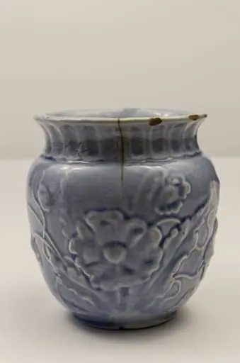 Piesă din faianță, cu aspect piriform, cu buza ușor evazată spre exterior, prevăzută cu toartă laterală semiovală. Decorul este reliefat și constă în motive florale (macul în diverse faze de dezvoltare: boboc, mac înflorit, capsule). Gâtul piesei este evidențiat printr-un brâu format din caneluri verticale. Cromatică: alb, bleu., by Unknown
