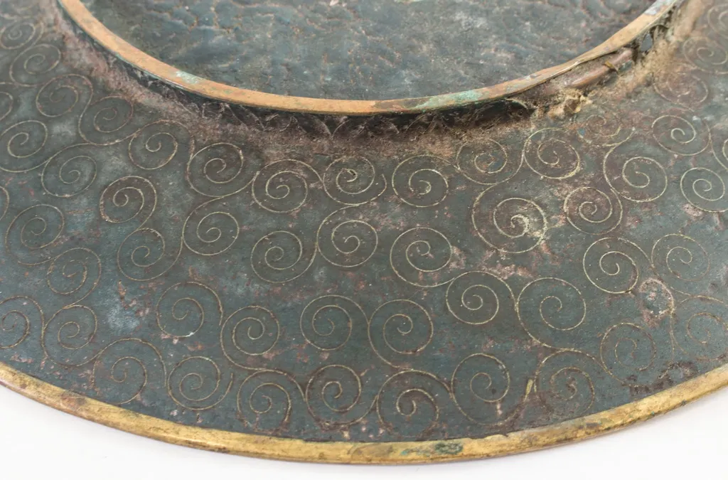 Piesă din metal pictat, incizat, de formă rotundă, puțin adâncită, cu fundul supraînălțat printr-un brâu circular. Decorul este dispus pe toată suprafața piesei, atât pe față (motive pictate: central, un buchet de crizanteme cu frunze, alături de fluturi; pe margine, un brâu circular cu motive de forma evantaiului), cât și pe spate (compoziție compactă de spirale incizate). Cromatică: albastru, verde, galben, negru, grena, roz, mov, violet, maro, alb., by Unknown, 1850