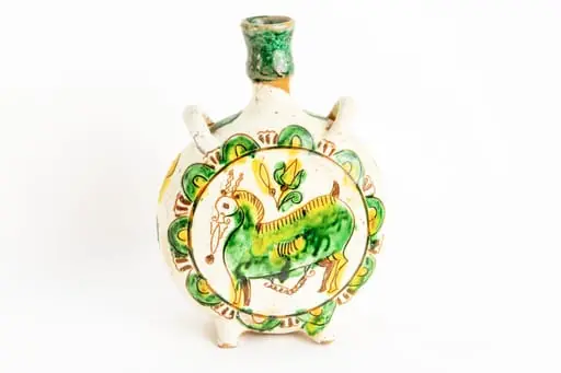 Ploscă circulară prevăzută cu două toarte în laterale pentru atașarea curelei. Fond alb. Pe fețele obiectului decorul este similar: un animal fantastic cu corp de culoare verde, cu contururi ușor zgrafitate, cu două coarne subțiri ușor ondulate de culoare maro deschis, cu un bot alungit, deasupra animalului este amplasată o lalea galbenă cu frunze galbene și verzi. Întreaga compoziție este înscrisă într-un cerc bordat de semicercuri de culoare verde cu interiorul galben. Pe muchia ploști sînt dispuse forme geometrice neregulate zgrafitate colorate în verde și respectiv galben. Gîtul ploștii este colorat cu verde., by Unknown