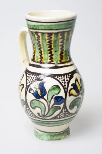 Recipient ceramic de formă ovoidală, smălțuit, cu gâtul lung, fund inelar și buza dreaptă. Prevăzut cu o toartă arcuită, care pleacă din mijlocul gâtului spre partea inferioară a vasului. Intens stilizat cu motive florale, vegetale și geometrice, pictate cu pensula, în două registre diferite. În primul registru, situat în zona gâtului, sunt pictate dungi late și linii meandrice dispuse pe verticală, alternativ. Aproape de gura vasului, sunt prezente dungi late și linii circulare. În al doilea registru întâlnim patru flori încadrate în cercuri și între acestea, puncte mici, umplând astfel cu decorații toată zona bombată a recipientului. Registrele sunt delimitate între ele de trei linii circulare. În partea inferioară, întâlnim ca și la gură, o dungă lată încadrată de două linii circulare. Prezent motiv geometric pe toartă sub formă de linie vălurită. Cromatică: fundal: alb; motive: galben; albastru; verde; maro închis., by Unknown