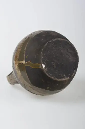 Recipient ceramic de formă sferică cu o toartă ce pornește de la baza buzei, printr-un inel, și se prinde de corp deasupra diametrului maxim. Buza este înaltă și relativ îngustă. Decorul este compus din motive geometrice (liniare, curbilinii) pictate, plasate pe toată suprafața obiectului. Pe alocuri sunt prezente pete de smalț. Vasul este smălțuit la exterior. Cromatică: fond: maron; bej; motive: maron închis, verde, galben., by Unknown