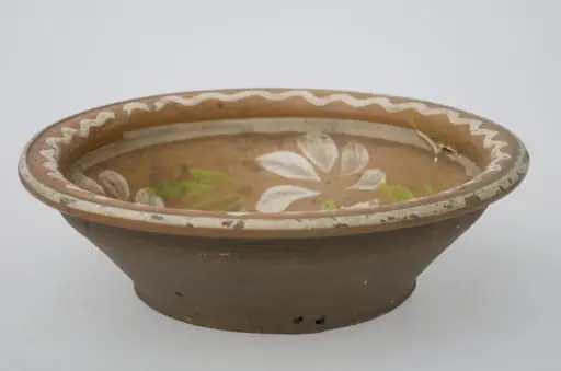 Vas adânc de formă tronconică, cu marginea bombată și evazată marcată de o linie în relief. Smălțuit numai în interior. Prezintă decor floral, iar pe margine două cercuri încadrează o linie frântâ. Cromatică: fond: cărămiziu; motive: alb, verde., by Unknown
